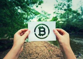 Woman hands holding a paper sheet with Bitcoin symbol in the middle of the nature with a river flowing near the forest. Eco crypto and digital currency concept.