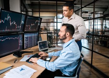 Two successful trader in formalwear working together in office, looking at screen, checking global currency index on fund exchange