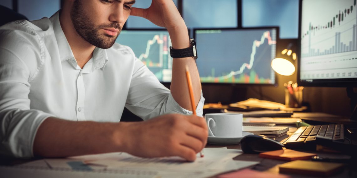 Serious businessman thinking hard of problem solution working late in office with computers documents, thoughtful trader focused on stock trading data analysis, analyzing forecasting financial rates
